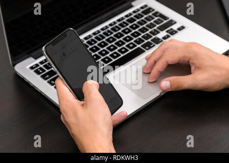 Mans Hände schreiben auf Smart Phone während der Arbeit am Laptop auf vintage Holztisch. Hände schreiben auf einer Tastatur. Ansicht von oben, Business Office Werkst Stockfoto