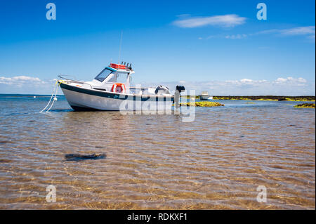 Weiße Boot auf Sand mit Wasser und Felsen im Sommer in Noirmoutier Stockfoto