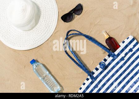 Strandtasche, Sonnencreme, Sonnenbrille und Hut auf Sand Stockfoto