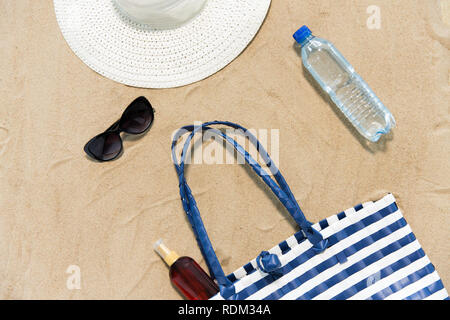 Strandtasche, Sonnencreme, Sonnenbrille und Hut auf Sand Stockfoto