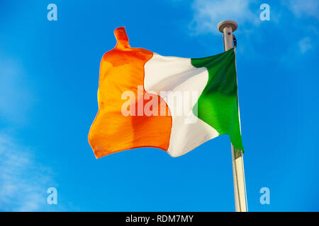 Die irische Flagge im Wind vor blauem Himmel. Stockfoto
