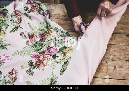 Hohen Winkel in der Nähe von Frau mit einer Schere rosa Stoff mit Blumenmuster zu schneiden. Stockfoto