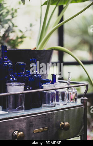 Nahaufnahme von klaren und blauen Gläsern und Flaschen auf vintage Metall Tisch mit Schublade. Stockfoto