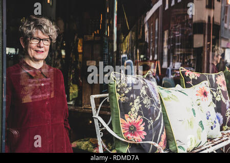 Lächelnde ältere Frau mit Brille und dem roten Kleid in Interior Design Store, bei Kamera schaut. Stockfoto