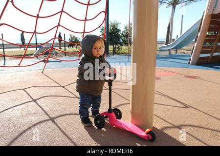 Cute Baby Junge spielt mit einem 3 Rad Roller auf einem Spielplatz. Nahaufnahme Portrait Stockfoto