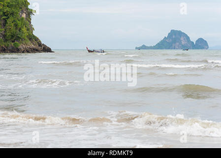 Meer in Ao Nang Strand während der windigen bewölkten Tag in der Nebensaison. Longtail Boote und eine Insel in der Ferne. Juli in Krabi, Thailand. Stockfoto