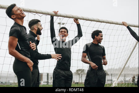 Fußballspieler stehen in der Nähe der Torpfosten und entspannen und lachen. Fußballer, die während eines Fußballspiels eine Pause machen, reden und lachen. Stockfoto