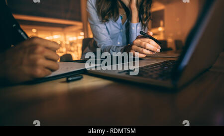 Nahaufnahme der Hände eines Geschäftsmannes und einer Geschäftsfrau, die Notizen macht und an einem Laptop arbeitet. Geschäftspartner, die spät im Büro sitzen und an einem Laptop arbeiten. Stockfoto