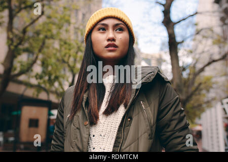 Nahaufnahme einer Frau im Winter Kleidung stehen im Freien. Asiatische Frau auf der Straße stand das Tragen einer Mütze und Wegsehen. Stockfoto