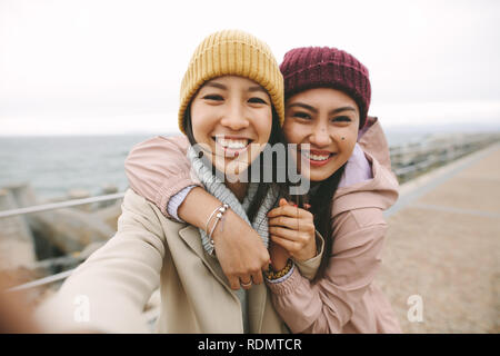 Freundliche asiatische Frau im Winter tragen, stehen in der Nähe des Meeres auf einem kalten Morgen. Lächelnde Frauen stehen im Freien jede andere Holding an einem Wintermorgen. Stockfoto