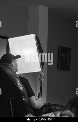 Junge Mann auf einem Stuhl sitzend mit einer Dose in der Hand mit einem weichen-box studio Lampe vor ihm Stockfoto