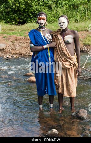 Zwei junge Frauen Surma mit Gesichts- und Körperbemalung durch den Fluss, Kibish, Omo-tal, Äthiopien, Afrika Stockfoto
