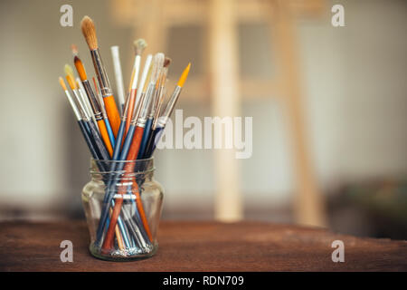 Glas mit Pinsel und Staffelei im Hintergrund Stockfoto