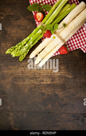 Zwei Bündel von frischen, rohen grünen und weißen Spargel Speere mit String auf eine geprüfte roten und weißen Tuch an rustikalem Holz mit Kopie Raum gebunden Stockfoto