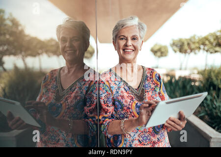 Porträt einer schönen grauen Haaren lächelnde Frau mittleren Alters arbeiten mit Tablette in die Kamera schaut Stockfoto