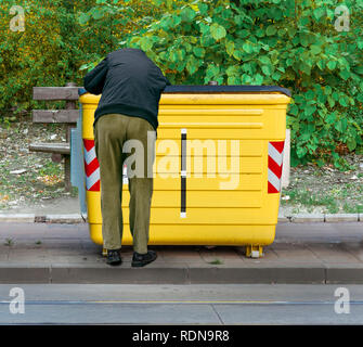 Mann graben sich durch den Müll in Gelb recycling Container auf der Straße Stockfoto