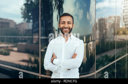 Portrait einer jungen zuversichtlich lächelnder Indischer Mann mit seinen Armen in die Kamera schaut gekreuzt Stockfoto