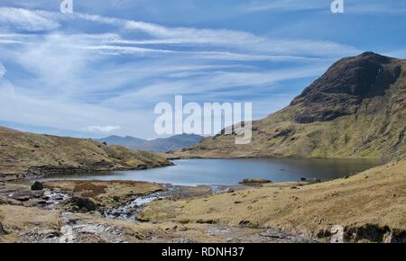 Schönen Berg Tarn (Kleiner See) an einem sonnigen Tag. Klippe, andere Berge in der Ferne. Stream und Fußweg im Vordergrund. Harrison Stickle, Stockfoto