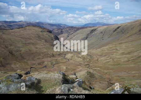 Ausblick In einem sumpfigen Tal, von einem fiel im englischen Lake District (Cumbria, UK). Felsen im Vordergrund und einem mäandernden Stream/riv Stockfoto