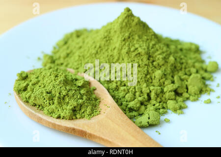Geschlossen bis ein Löffel von Vibrant Green Matcha Tee Pulver auf einem Teller mit verschwommenen Grünteepulver Haufen im Hintergrund Stockfoto
