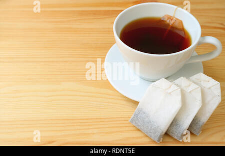 Teebeutel und eine Tasse frisch gebrühten heißen Tee mit Teebeutel auf hölzernen Tisch serviert Stockfoto