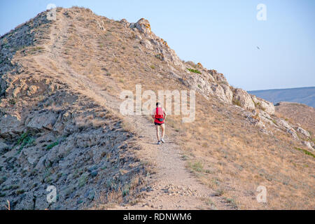 Ansicht der Rückseite des athletischen Runner läuft auf einem Berg trail auf einem blauen Himmel Hintergrund Stockfoto