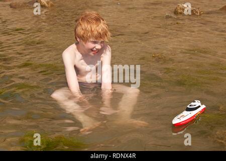 Junge sitzt im Meer, sein Spielzeug Boot spielen, Timmendorf, Insel Poel, Norddeutschland, Ostsee Stockfoto