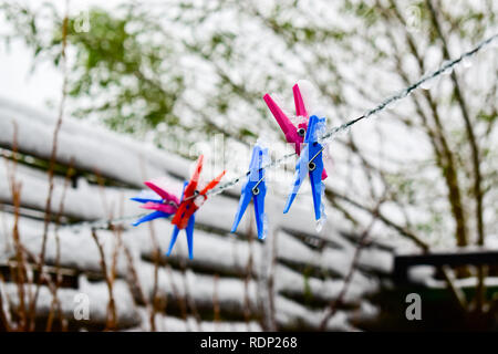 Eisige farbige Clips zur Befestigung Wäscheservice, gefrorene Schnur und verschwommenes Winter Hintergrund. Stockfoto