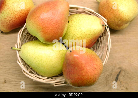 Rote und gelbe Birnen legt in kleinen Korb Stroh Korb auf braune Holztisch Draufsicht closeup Stockfoto