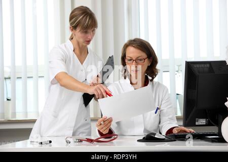 Die medizinische Praxis, Arzt Untersuchung der Gesundheitsdaten eines Patienten an ihrem Schreibtisch, Sie diskutieren mit einem Assistenten Stockfoto