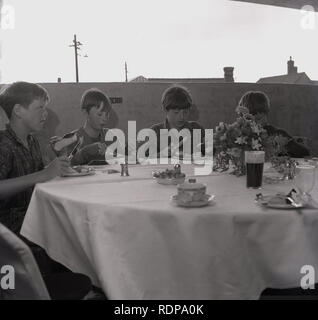 1967, historische, vier junge Jungen, die einen ausgefallenen Tee auf einem mit Stoff bedeckten Tisch an einem ungewöhnlichen Ort haben... die oberste Etage eines mehrstöckigen Parkplatzes, organisiert vom gemeinderat zur Feier seiner Eröffnung, England, Großbritannien. Stockfoto
