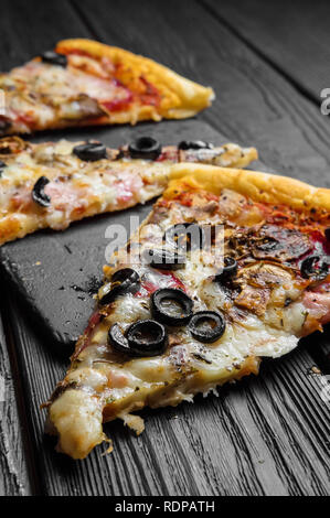 Stück Pizza auf dunklen schwarzen Holzplatte, traditionelle italienische Pizza Stockfoto