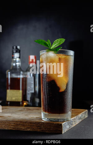 Glas Cola mit Eis, Minze und Rosmarin auf schwarzem Hintergrund Stockfoto