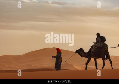 Berber tribesman führt eine Kamelkarawane durch die hohen Dünen der Wüste Sahara. Stockfoto