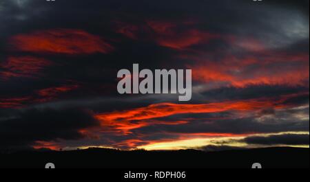 Einen atemberaubenden Sonnenuntergang mit roten Wolken gegen einen Sturm grauer Himmel. Über Dartmoor, Devon. Stockfoto