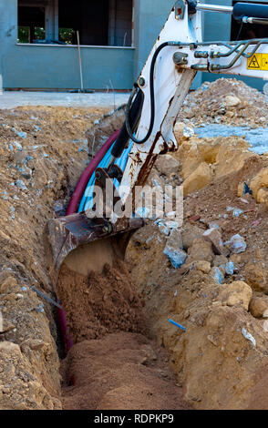 Bagger elektrische Leitungen mit Hilfe eines Arbeitnehmers mit Sand bedeckt. Stockfoto