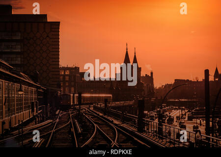 Berliner Stadtbild bei Sonnenuntergang mit dem Zug über Oberbaumbrücke zwischen Kreuzberg und Friedrichshain. Stockfoto