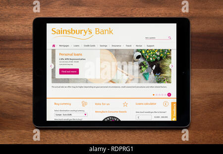 Die Website von Sainsbury's Bank gesehen auf einem iPad Tablet, der ruht auf einem Holztisch (nur redaktionelle Nutzung). Stockfoto