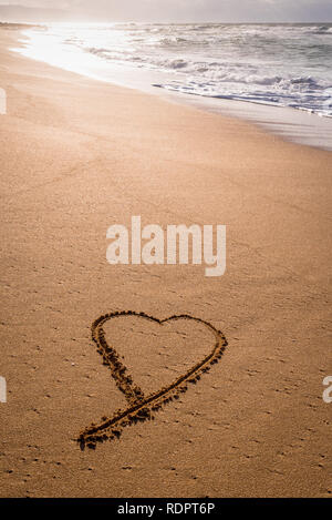 Herz im Sand am Strand bei Sonnenuntergang mit Wellen Waschmaschine angesaugt Stockfoto