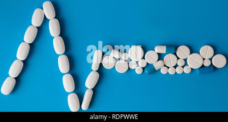 Arzneimittel weiße, runde herzförmige Pillen auf blauem Hintergrund isoliert. Tabletten in Form einer Linie des Herzrhythmus auf einem Pastell-blaue Hintergrund. Ca Stockfoto