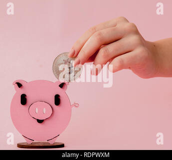 Nahaufnahme Hände von Frau setzen gold Bitcoin rosa Sparschwein, mit Kopie Platz für Banner Design, geringe Tiefenschärfe, wählen Sie Fokus auf der Hand. Stockfoto