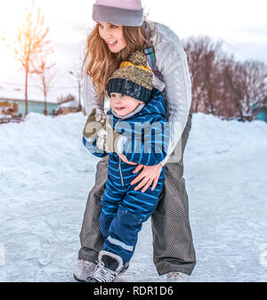 Mädchen einen kleinen Jungen zu halten. Im Winter, City Skate. Vorderansicht. Schwester mit ihrem Sohn lernt zu Skate auf Skates stehen und. Stockfoto