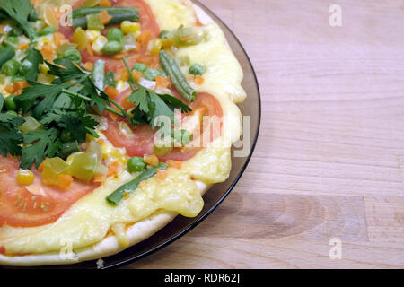 Fragment der gekochten appetitliche Pizza mit Tomaten, mais und Erbsen auf runden Platte auf Holz- Hintergrund der Ansicht von oben Stockfoto