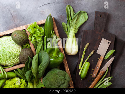 Sortiert grün getönten roh Bio Gemüse im Holzkasten auf dunklem Stein Hintergrund. Avocado, Kohl, Blumenkohl und Bohnen und Gurken mit getrimmt Stockfoto
