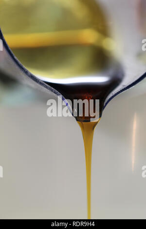 Gießen Sirup aus einem Messbecher auf eine weiße Schüssel. Der Sirup ist wunderschön golden/braune Flüssigkeit. Dies ist ein schließt/Makro Foto über backen. Stockfoto