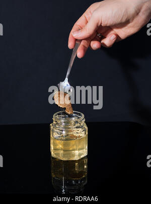 Trüffel Pilz in ein Glas Honig auf schwarzem Hintergrund. Minimalismus in der Komposition. Luxus essen. Freier Platz für Text Stockfoto