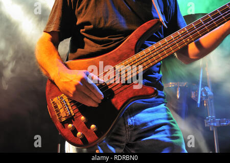 E-Bass Gitarre Spieler spielt auf der Bühne mit Rauch und Licht in der Nähe von dem Zupfen der Saiten mit Daumen Stockfoto