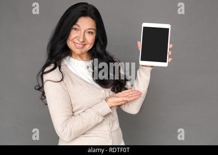 Freestyle. Reife Lady stehen isoliert auf grau angezeigt Bildschirm digitaler Tablet freundlich Stockfoto