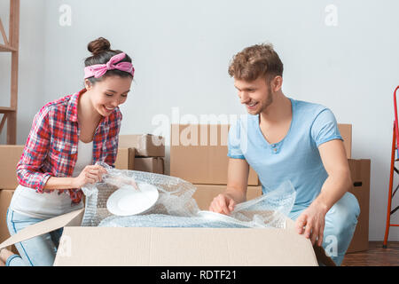 Junges Paar, der seinen neuen Platz sitzen in der Nähe von Box auspacken Gerichte lächelt glücklich Stockfoto