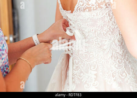 Brautjunfer Vorbereitung der Braut für die Hochzeit. Brautjunfer helfen Braut befestigen Sie Ihre Hochzeit weiß Kleid mit Schnürung vor der Zeremonie. Luxus Brautkleid schließen Stockfoto